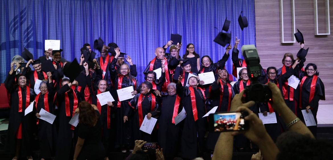 Turma de formandos da UATI reunidos no palco e apresentando seus diplomas de graduação.