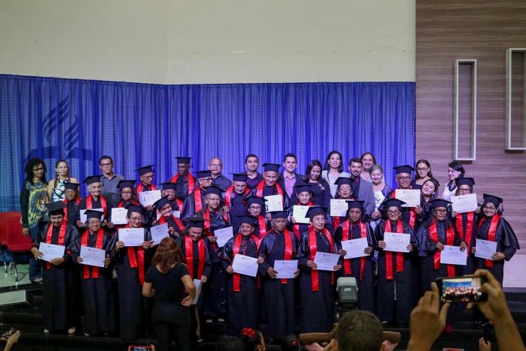 Turma de formandos da UATI reunidos no palco e apresentando seus diplomas de conclusão graduação.
