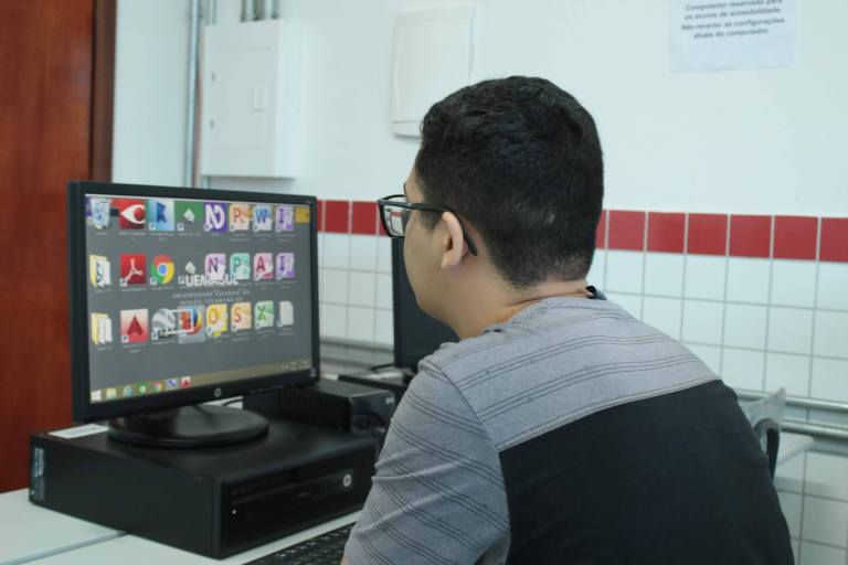 Acadêmico com baixa visão utiliza computador com ícones de programas aumentados.