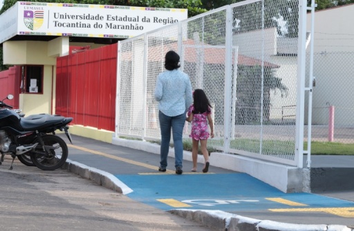 Uma mulher adulta caminha pela calçada tátil da UEMASUL de mãos dadas com uma criança.